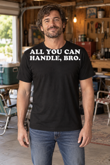 AI-generated lifestyle visualization: person wearing the black tri-blend All You Can Handle, Bro. quote T-shirt in a lived-in rec-room garage