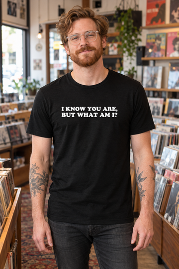 AI-generated lifestyle visualization of a hipster man wearing the black tri-blend I Know You Are, but What Am I? quote T-shirt in an independent record store