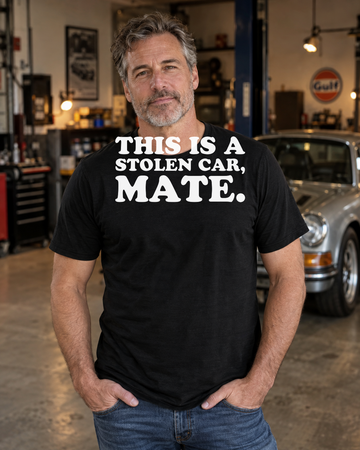 AI-generated lifestyle visualization of a person wearing the This Is a Stolen Car, Mate. black tri-blend quote T-shirt in a classic-car garage
