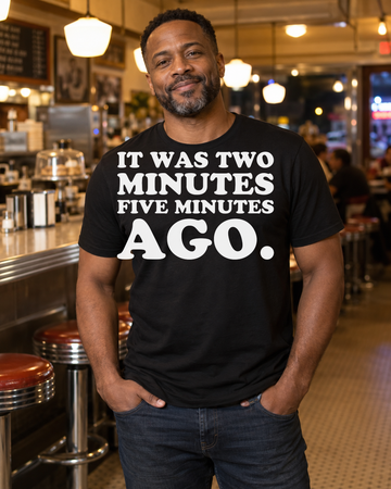 AI-generated lifestyle visualization of a person wearing the It Was Two Minutes Five Minutes Ago. black tri-blend quote T-shirt in a neighborhood diner