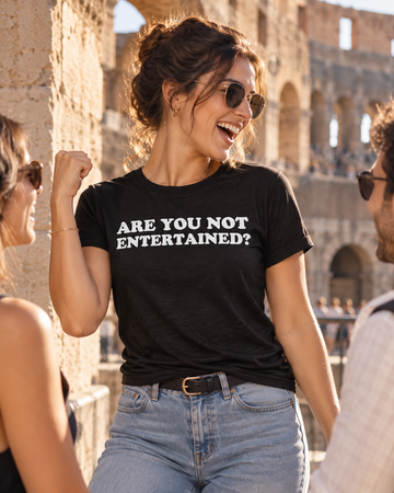 AI-generated lifestyle visualization: person wearing the black tri-blend Are You Not Entertained? quote T-shirt in an old stone amphitheater concourse in strong late-afternoon sunlight