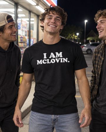 AI-generated lifestyle visualization: person wearing the black tri-blend I Am McLovin. quote T-shirt in a late-night convenience store exterior with fluorescent light and a quiet suburban parking lot
