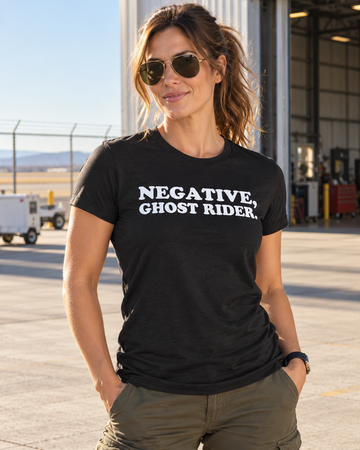 AI-generated lifestyle visualization: person wearing the black tri-blend Negative, Ghost Rider. quote T-shirt in sunlit aircraft hangar exterior with runway fencing, utility vehicles, and no military insignia
