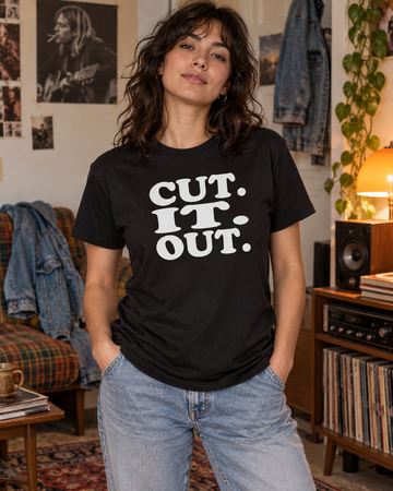 AI-generated lifestyle visualization: person wearing the black tri-blend Cut. It. Out. quote T-shirt in a casual 1990s apartment hangout with denim jackets, a stereo cabinet, and warm practical light