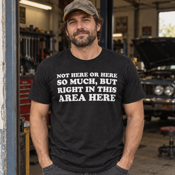 AI-generated lifestyle visualization: person wearing the black tri-blend Not Here or Here So Much, But Right in This Area Here quote T-shirt at an auto garage