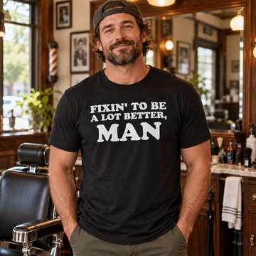 AI-generated lifestyle visualization: person wearing the black tri-blend Fixin' to Be a Lot Better, Man quote T-shirt in a neighborhood barbershop