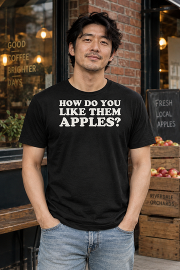 AI-generated lifestyle visualization: person wearing the black tri-blend How Do You Like Them Apples? quote T-shirt in brick-lined neighborhood cafe exterior with apple crates and relaxed 1990s street style