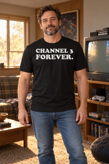 AI-generated lifestyle visualization of a person wearing the black tri-blend Channel 3 Forever. quote T-shirt in wood-paneled retro rec room with an adult man beside a generic CRT television, warm practical light, no visible brands, and the full blank black T-shirt front unobstructed