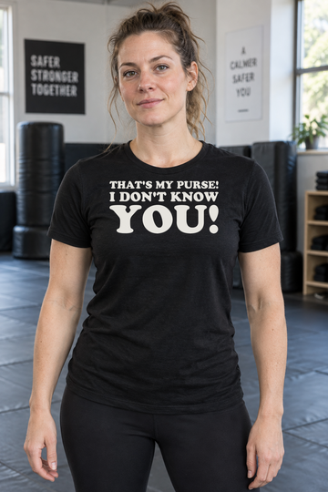 AI-generated lifestyle visualization: person wearing the black tri-blend That's My Purse! I Don't Know You! quote T-shirt in suburban community self-defense class with gym mats, natural light, and no character imagery