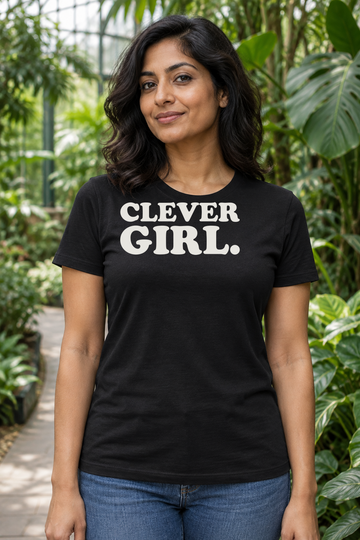 AI-generated lifestyle visualization: person wearing the black tri-blend Clever Girl. quote T-shirt in lush botanical conservatory walkway with dramatic leaves and no dinosaur or franchise imagery