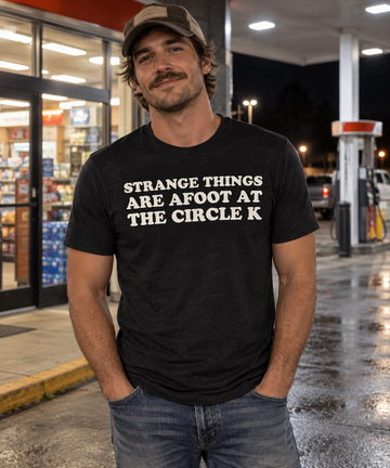 AI-generated lifestyle visualization: person wearing the black tri-blend Strange Things Are Afoot at the Circle K quote T-shirt outside a late-night convenience store