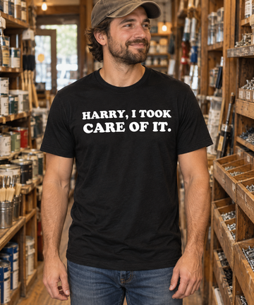 AI-generated lifestyle visualization: person wearing the black tri-blend Harry, I Took Care of It quote T-shirt in a neighborhood hardware store