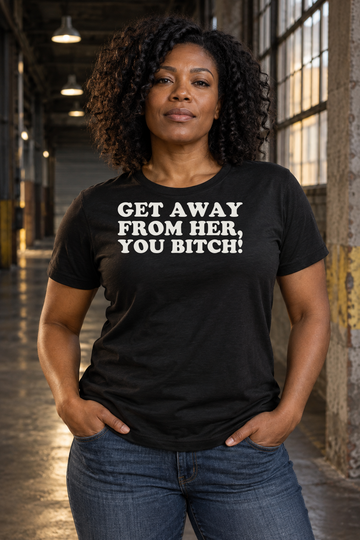 AI-generated lifestyle visualization: person wearing the black tri-blend Get Away from Her, You Bitch! quote T-shirt in industrial warehouse corridor with dramatic practical lighting and no science-fiction costumes or franchise imagery