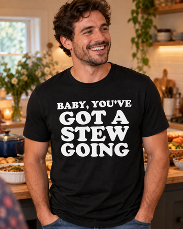 AI-generated lifestyle visualization: person wearing the black tri-blend Baby, You've Got a Stew Going quote T-shirt at a kitchen gathering