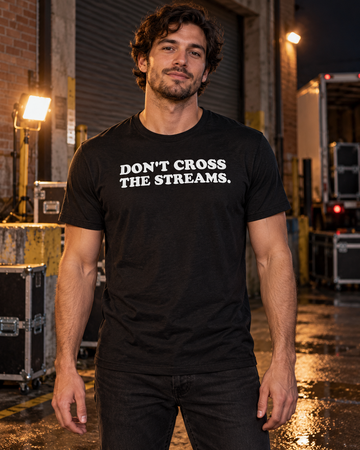 AI-generated lifestyle visualization: person wearing the black tri-blend Don't Cross the Streams. quote T-shirt in a 1980s downtown loading dock at night with utility cases, practical work lights, and no licensed props