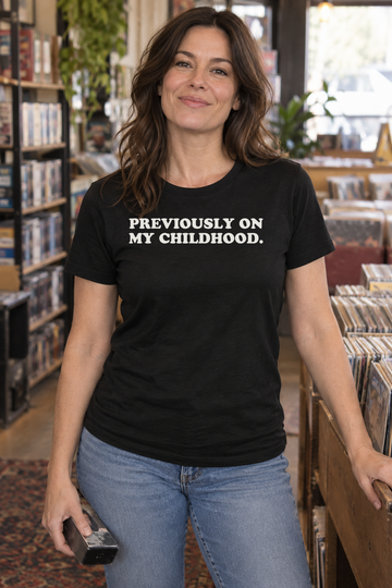 AI-generated lifestyle visualization of a person wearing the black tri-blend Previously on My Childhood. quote T-shirt in casual record and media shop with a different adult model flipping through a generic VHS bin, soft afternoon light, no brands, and the black T-shirt front unobstructed