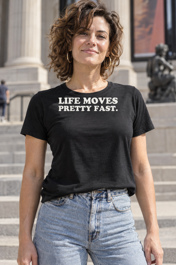 AI-generated lifestyle visualization: person wearing the black tri-blend Life Moves Pretty Fast. quote T-shirt in sunny downtown museum steps with late-1980s styling and no recognizable logos or landmarks