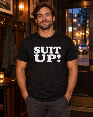 AI-generated lifestyle visualization: person wearing the black tri-blend Suit Up! quote T-shirt in a warm neighborhood bar entry with coat hooks, dark wood, and evening city light through the window