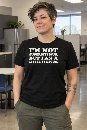 AI-generated lifestyle visualization: person wearing the black tri-blend I'm Not Superstitious. But I Am a Little Stitious. quote T-shirt in ordinary office break room with neutral cubicles and no show-specific props or logos