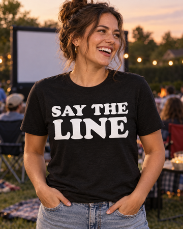 AI-generated lifestyle visualization: person wearing the black tri-blend Say the Line. Find Your People. Quote Club T-shirt at an outdoor movie night