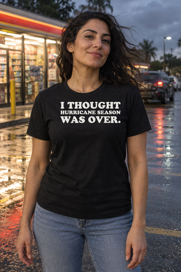 AI-generated lifestyle visualization: person wearing the black tri-blend I Thought Hurricane Season Was Over. quote T-shirt in windy neighborhood convenience-store parking lot after rain with no visible brands