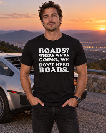 AI-generated lifestyle visualization: person wearing the black tri-blend Roads? Where We're Going, We Don't Need Roads. quote T-shirt in a retro roadside overlook at dusk with a parked stainless sports car silhouette and no visible branding