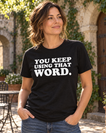AI-generated lifestyle visualization: person wearing the black tri-blend You Keep Using That Word. quote T-shirt in old stone courtyard with climbing ivy, warm afternoon light, and understated storybook atmosphere