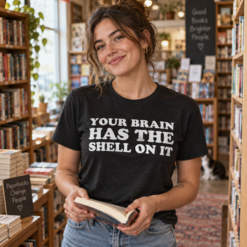 AI-generated lifestyle visualization: person wearing the black tri-blend Your Brain Has the Shell on It quote T-shirt in an independent used bookstore