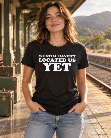 AI-generated lifestyle visualization: person wearing the black tri-blend We Still Haven't Located Us Yet quote T-shirt at a vintage train platform