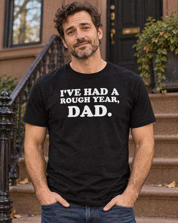 AI-generated lifestyle visualization: person wearing the black tri-blend I've Had a Rough Year, Dad. quote T-shirt in a quiet brownstone stoop on a cool city afternoon with centered framing and subdued fall colors