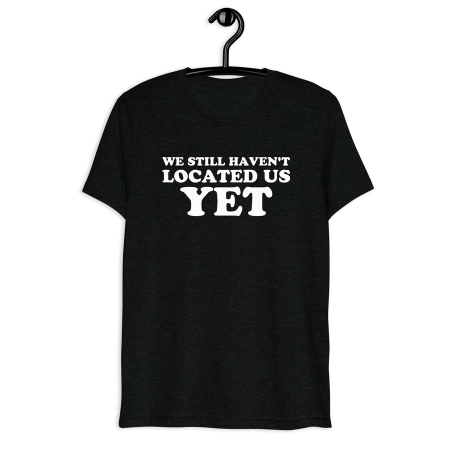 Front hanger view of black tri-blend quote shirt reading We Still Haven't Located Us Yet