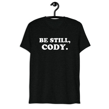 Front hanger view of black tri-blend quote shirt reading Be Still, Cody.