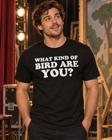 AI-generated lifestyle visualization: person wearing the black tri-blend What Kind of Bird Are You? quote T-shirt in a 1960s community theater backstage with painted bird costumes and warm work lights