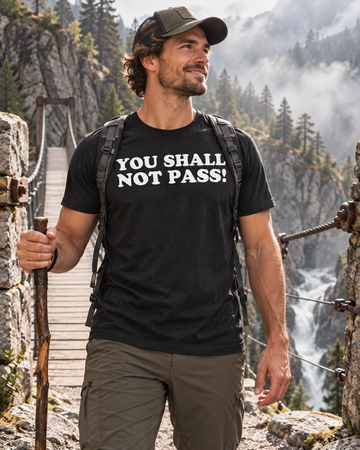 AI-generated lifestyle visualization: person wearing the black tri-blend You Shall Not Pass! quote T-shirt in a rocky mountain footbridge with misty natural light and deep stone textures